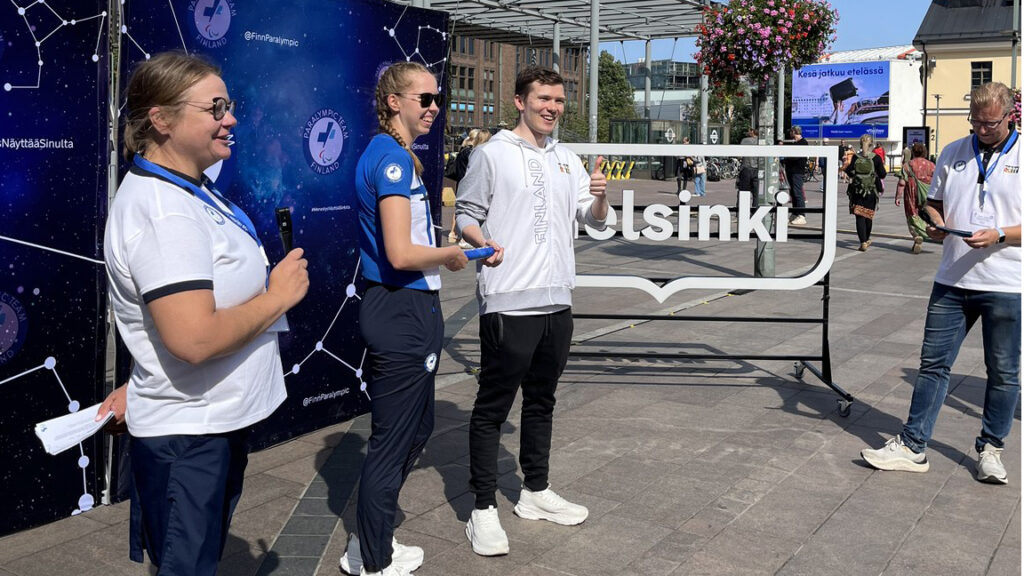 Olympiaurheilija, sulkapalloilija, Kalle Koljonen ojentamassa ''vaihtokapulaa'' paralympiaurheilija, yleisurheilija, Iida Lounelalle.